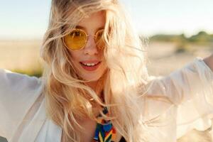 Close up portrait of blonde girl playing with hairs, having fun and enjoying summer on the beach. photo