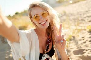 Close up portrait of smiling woman with blonde hairs making self portrait on sunny evening beach. photo