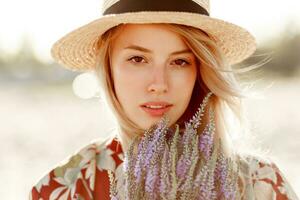 Romantic happy close up portrait of charming blonde girl in straw hat smells flowers on the beach. photo
