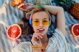 Excited girl on beach towel. Boho accessories. Tropical fruits. Yellow sunglasses.Top view. photo