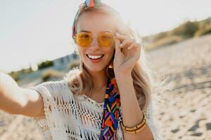 Happy positive mood. Blond playful girl with stylish headband making self portrait on tropical sunny beach. Travel and freedom concept. Bohemian outfit. photo