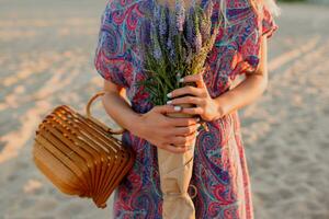 al aire libre verano imagen mujer en vistoso vestir caminando en el playa con ramo de flores de lavanda. foto