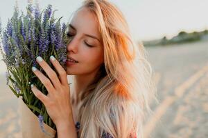 Beauty portrait of romantic blonde woman with bouquet of lavender looking at camera on the beach. photo