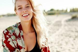 Excited blond woman with perfect smile having fun and looking at camera on sunny white sand beach. photo