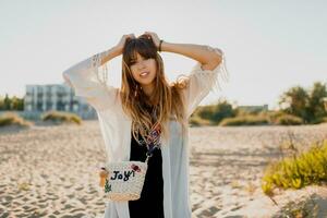 romántico niña con largo pelo caminando en el playa. bohemio estilo, Paja bolso brillante hacer arriba. foto