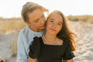 Outdoor   portrait  of beautiful family. Mother and doughter posing on the beach. Warm sunset colors. photo