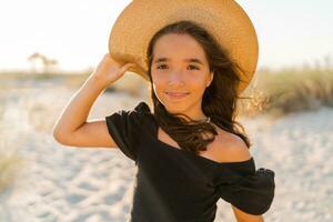 Cute small girl in stylish linen dress and straw hat posing on the beach. Sunset warm colors. photo