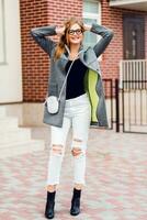 Fashion image of stylish blond woman in grey coat walking on the street. Full lenght. photo