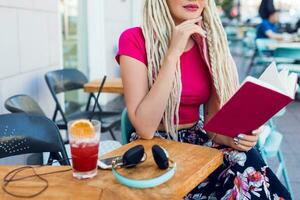 Unusual blonde woman with dreadlocks sitting in cafe. Wearing bright  pants with tropical print. photo