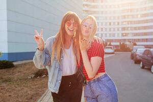Two joyful women  having fun outdoor. Stylish jeans jacket with print. Urban background . photo