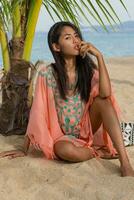 increíble sexy bronceado asiático mujer posando en paraíso tropical playa debajo el pam árbol. foto