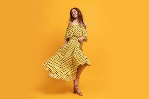 Pretty red-head woman in yellow dress posing in studio. Summer mood. Full lenght. photo