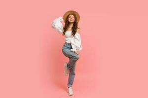 Full lenght image of Ppayful  woman in elegant linen top with balloon sleeves and blue jeans posing on pink background.  Summer fashion trends. photo