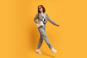 Stylish teen woman in casual outfit and trendy sunglasses posing  on yellow background in studio. Autumn style.  full length photo