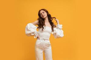 Sexy elegant woman in white blouse and trousers posing on yellow background in studdio. Summer fashion trends. photo