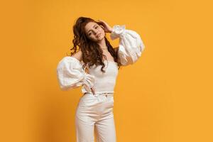 Fashion studio photo of pretty red haired woman in white elegant clothes posing on yellow background.