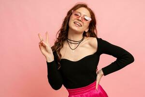 Beautiful red  head  woman  in suglasses posing over pink background. Wavy hairs. Perfect smile.  Isolate in studio. photo