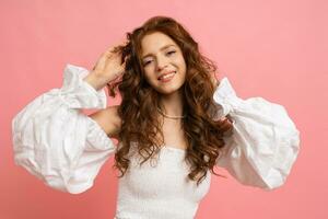 estudio retrato de encantador rojo peludo mujer en blanco parte superior con mangas en rosado antecedentes. foto