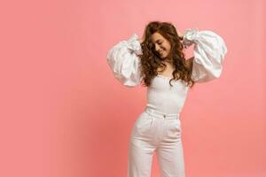 Fashion studio photo of elegant red haired   woman in  white summer outfit  with  sleeves over pink background.