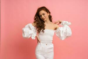 Fashion studio photo of elegant red haired   woman in  white summer outfit  with  sleeves over pink background.