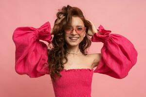 Stylish red-haired woman posing in pink lien dress with  sleeves over pink background. photo