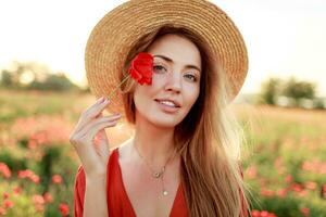 Close up portrait of lovely young romantic woman with poppy flower in hand posing on field. photo