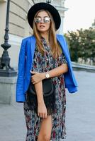 Fashionable  girl in elegant  autumn outfit walking while holidays in Europe. Stylish leather bag.  Blue jacket and black hat. photo
