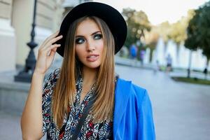 agraciado niña en elegante otoño atuendo caminando mientras Días festivos en Europa. elegante cuero bolsa. azul chaqueta y negro sombrero. foto