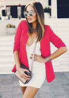 mujer con brillante hacer arriba, blanco vestir y rosado chaqueta, posando en calle . de moda casual complementa , mano bolso . foto