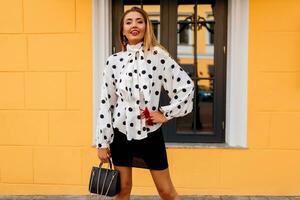 Outdoor image of lovable happy woman in stylish spring clothes with luxury  bag posing on the street over yellow background. photo