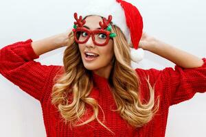 Joyful carefree blond woman in cute masquerade glasses and new year hat in red knitted sweater posing on white background . Isolate. Christmas and new test party concept. photo