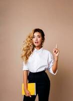 Blond business woman pointing up and looking at camera on beige background. Wearing stylish workwear. Copy space fo text.  Surprise face. photo