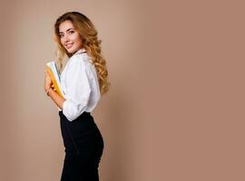 Businesswoman in stylish eyeglasses standing over beige wall. Blond wavy hairs. White blouse and  black trousers. photo