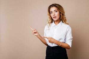 Blond business woman pointing up and looking at camera on beige background. Wearing stylish workwear. Copy space fo text. photo