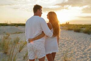 joven europeo Pareja en amor disfrutando romántico noche en el playa, abrazando y acecho el puesta de sol. foto