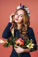 Spring romantic  fashion portrait beautiful young female with long wavy blonde  hair in wreath of spring flowers  posing with flower bouquet over   pink  background. photo