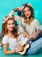 Funny fashion girls  posing on blue wall background in summer style outfit with  flowers  wreath wearing blue jeans and boho bag pack. . photo