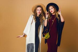 two models  with blond wavy hairstyle in wool and straw hat wearing striped poncho. American or Australian hippie bohemian style. Girls laughing  and  enjoying  time . photo