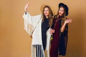 two models  with blond wavy hairstyle in wool and straw hat wearing striped poncho. American or Australian hippie bohemian style. Girls laughing  and  enjoying  time . photo