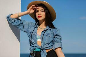 Stunning  woman with perfect figure in sexy shorts and straw hat posing on the beach. Blue sky and sea on background. photo