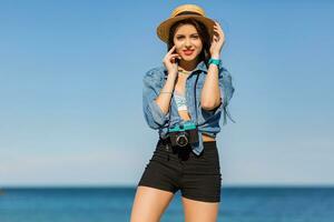 Sexy woman with perfect tan body, full red lips and l  long legs posing on the  tropical  sunny beach. Wearing  crop top , shorts and straw hat. Bright sunny colors. photo