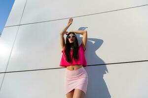 elegante mujer en verano ropa y Gafas de sol posando terminado blanco urbano antecedentes. foto