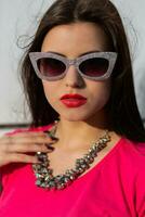 Close up portrait of fashionable brunette woman in stylish sunglasses and pink t-shirt. photo