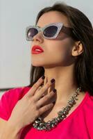 Close up portrait of fashionable brunette woman in stylish sunglasses and pink t-shirt. photo