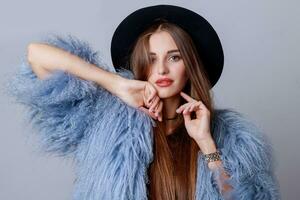 Close up indoor studio fashion portrait of pretty young model in stylish winter fluffy coat and black hat. photo