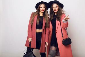 Two attractive young models  in casual spring outfit, pink coat . Fashion trendy look. Bright  make up. Brunette  long hairs. photo