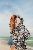 Carefree woman jumping freedom on white sand. Blue ocean background. Windy hairs. photo