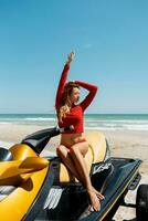 Young sexy blond woman with perfect body  in  red  outfit  sitting on water scooter on  the beach  in a sunshine. Summer weekend or vacation. Extreme sport. photo