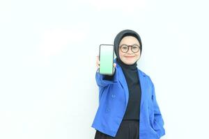 smiling beautiful asian women in blue blazer and hijab showing green screen mobile phone photo
