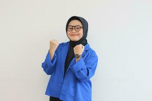 beautiful young Asian Muslim woman, wearing glasses and blue blazer with fists clenched in spirit gesture photo